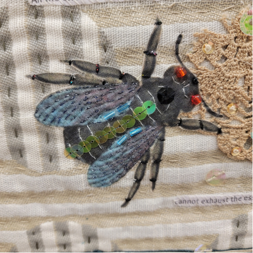 A decorative bee made with beads, sequins, and fabric is placed on a textured, patchwork background with crochet and stitched elements.